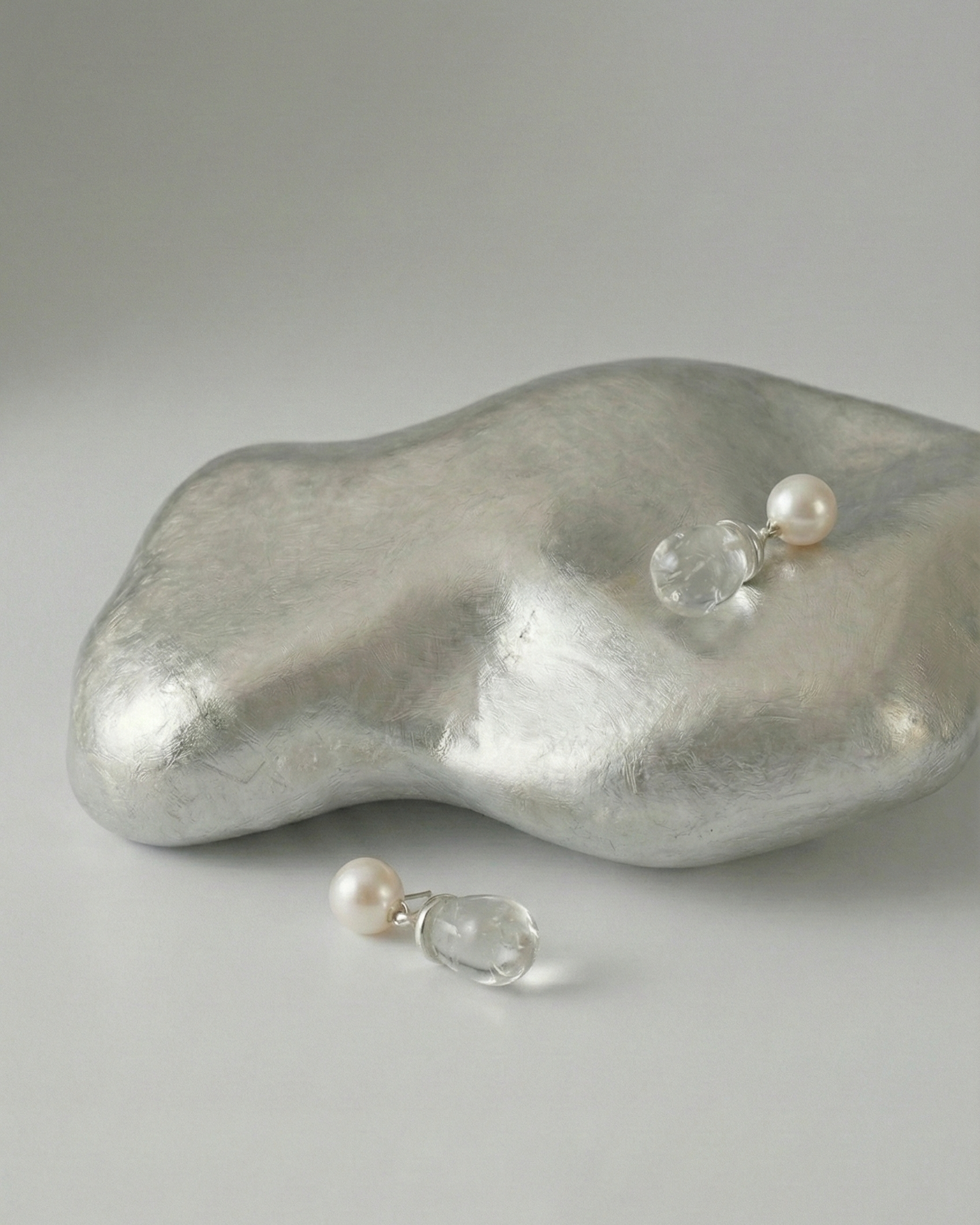 Pearl earrings with clear gemstones on a textured silver surface