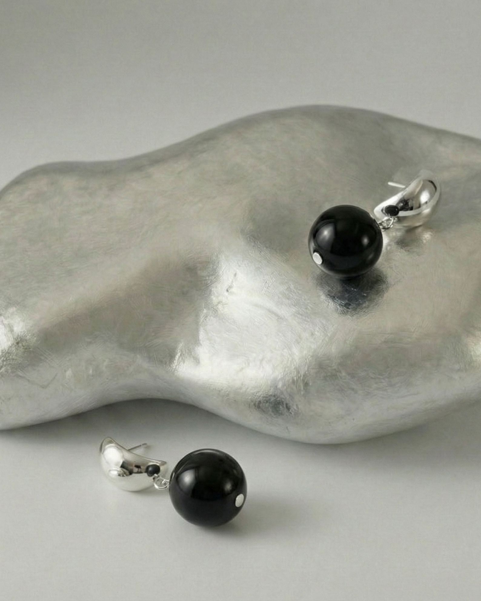 Black bead earrings on a textured silver surface